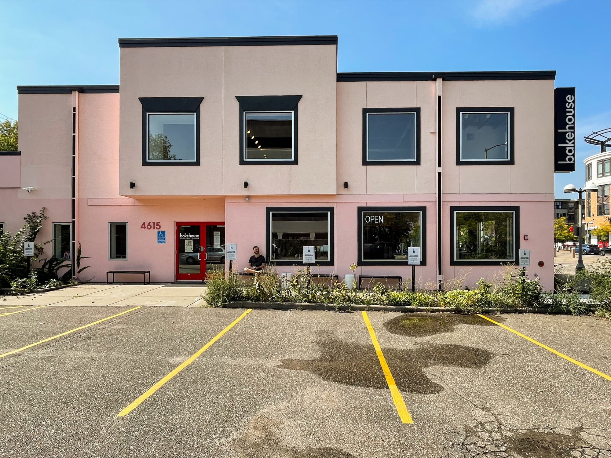 Two-story pink bakehouse building with red entry doors and a parking lot