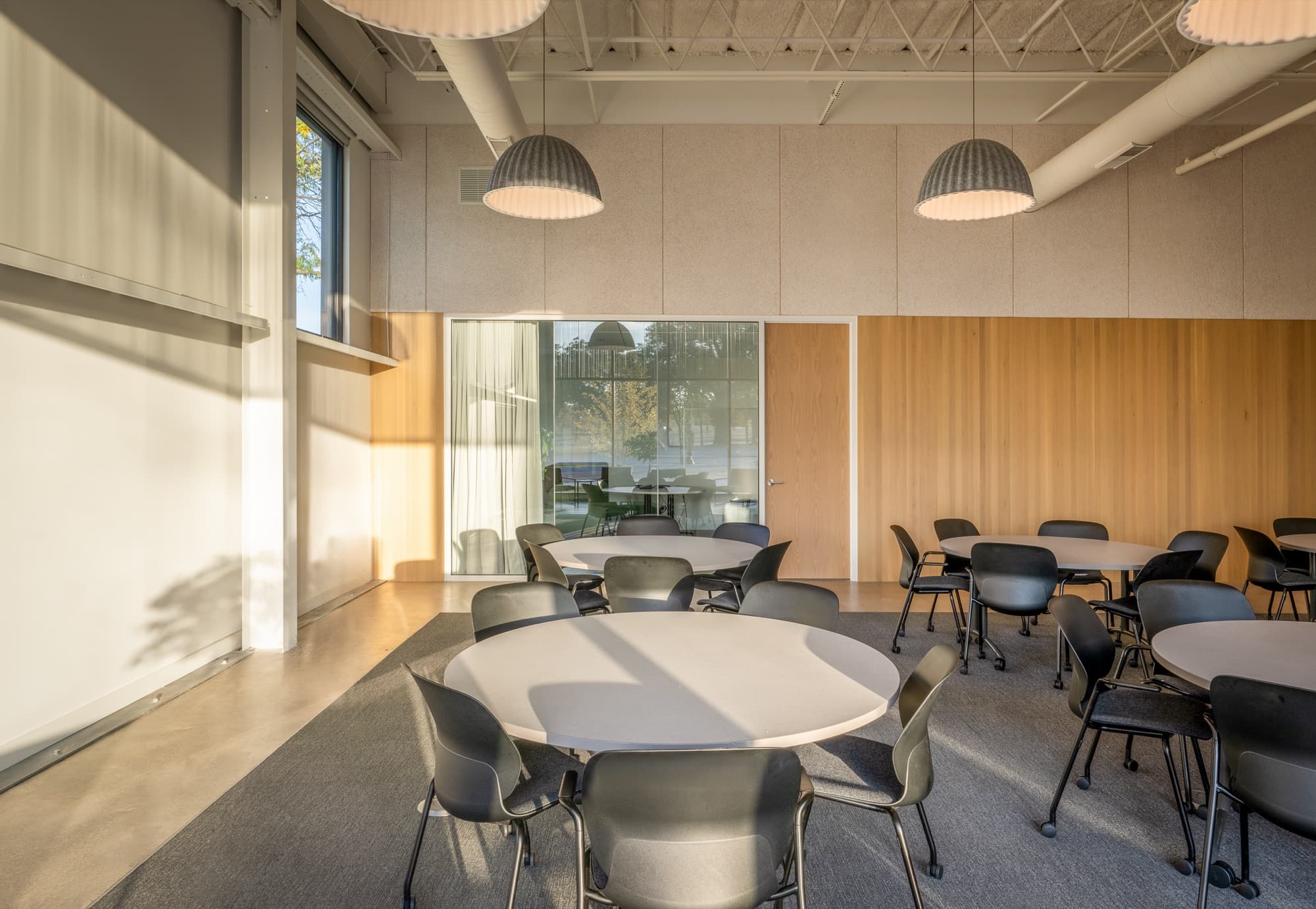 Dining area with round tables under pendant lights and a wood-clad wall